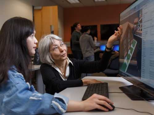 Female professor with students in front of desktop computer