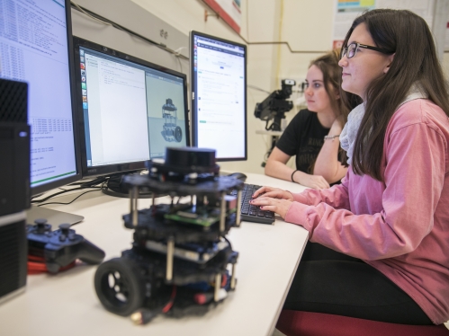 Two female students collaborating looking at three desktop screens.