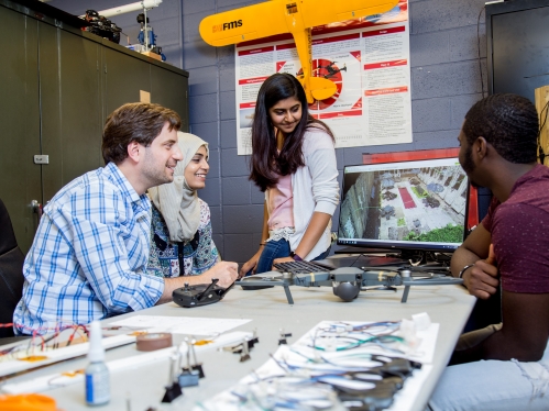 Professor working with three students in drone lab in front of desktop