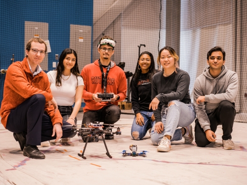 Group of students kneeling with professor in aerospace lab