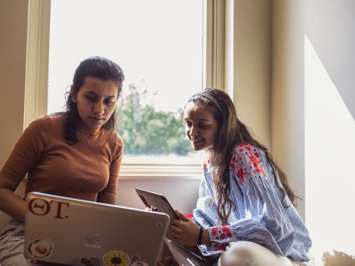 two female students sitting in front of window looking at laptop