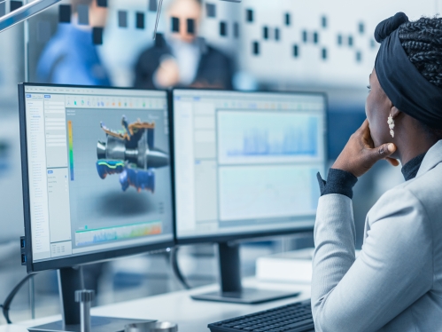 woman in white shirt and black braids tied up with a black scarf studies content on a computer monitor