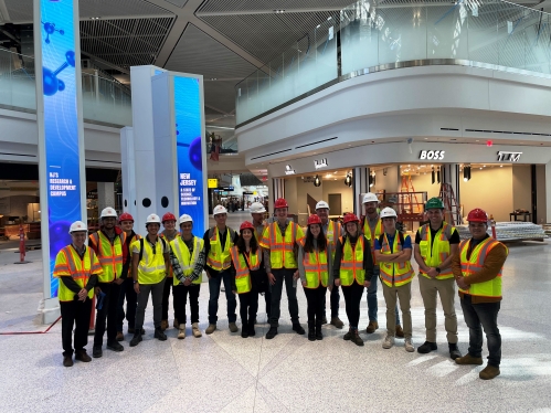 Group of students in hard hats and construction vests visit job site.