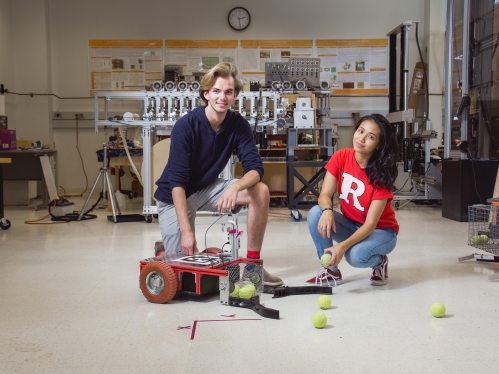 Male and female students knelling alongside a tennis ball collection device.