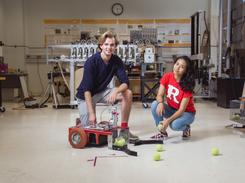 Male and female students knelling alongside a tennis ball collection device.