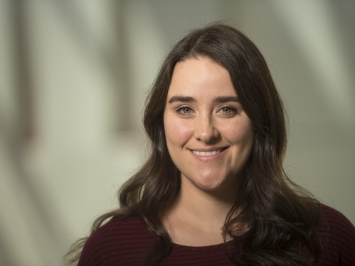 Young woman with dark hair smiling, filtered light behind her.