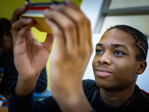 Young smiling black male focusing on his project he is holding close to his face. 