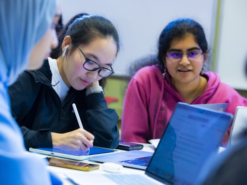 Two Asian females with dark hair and eyeglasses use their laptops to study in the Busch Learning Center