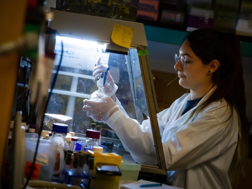 female student wearing eyeglasses in a white lab coat working with pipette