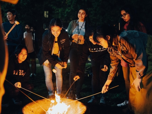 Students around campfire roasting marshmallows.