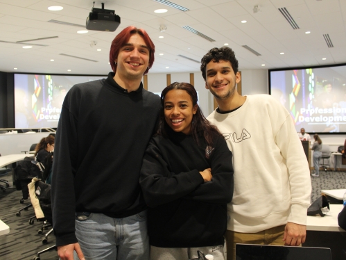 A tall male student, a Black female student, and another male student smile and pose for the camera. 