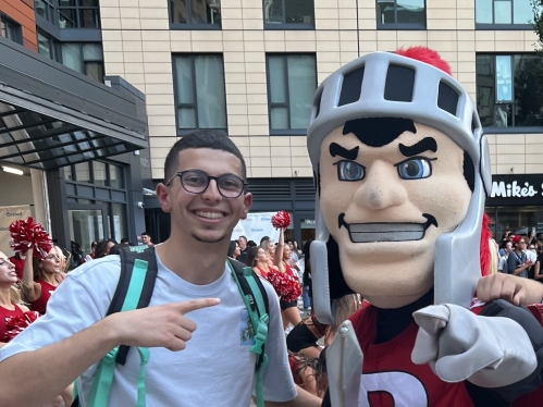 Young man wearing shorts and a T-shirt poses with the Rutgers Scarlet Knight mascot.