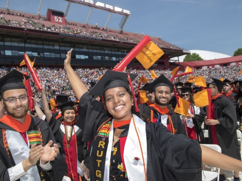 Group of male and female students in regalia celebrating their graduation in the stadium.