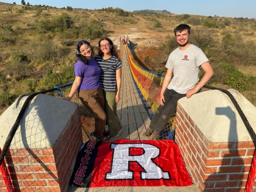Two femal and one male student standing on a bridge the help build in Africa.