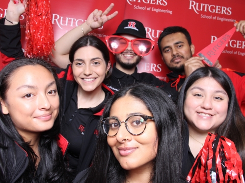 Group of six college students posing in front of Rutgers banner.