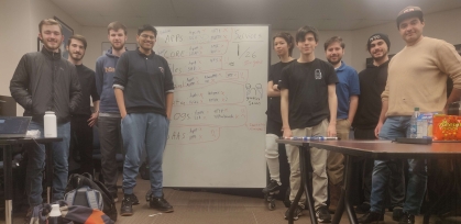 Eight students standing on either side of a white board along with their advisor