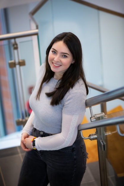 Smiling female student with long black hair standing on staircase looking up at the camera