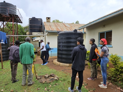 A group of students and local village members inspect water tower in Africa.