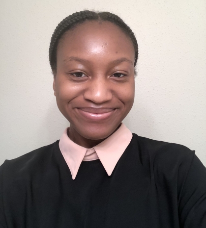 Head shot of female African American undergraduate student, smiling wearing a pink blouse under a black sweater. Her hair is parted in the middle and tied back.
