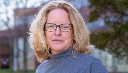Head shot of white female with eyeglasses, shoulder length blonde hair and wearing a light blue turtle neck sweater. 