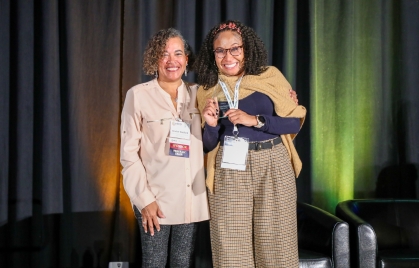 Two women pose together, one holding an award. 