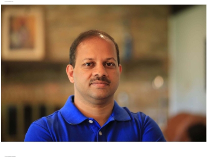 Head shot of Indian male with dark moustache, and wearing a blue button down shirt.