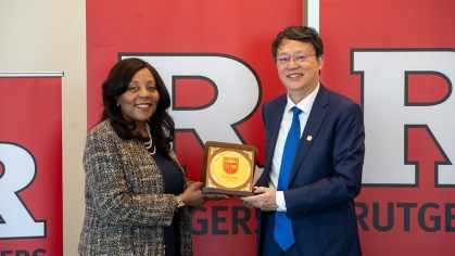 Woman and man pose holding a plaque in front of a Rutgers banner.