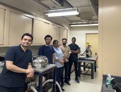 Male professor poses in his labe with four students.
