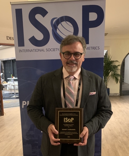 Man with gray hair and glasses wearing a suit and tie, poses with an award plaque in front of a banner that says ISOP.