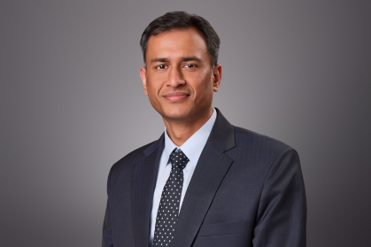 Headshot of male wearing a dark blue suit, light blue shirt, and dark blue tie.
