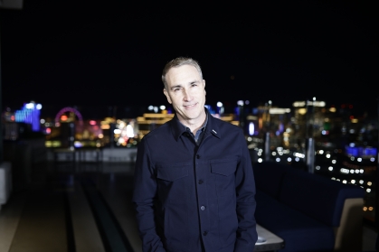 Man standing against a night skyline wearing a dark shirt and smiling.