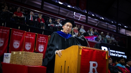Man in graduation regalia delivers address from a podium.