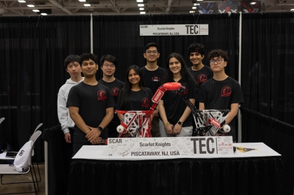 Eight students pose in front of a table with their robotic device.