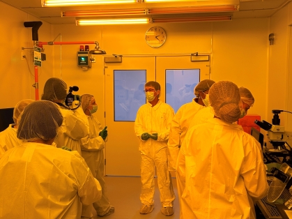 A group of people gather in a lab. They are all wearing white protective suits, masks, and hair covering.