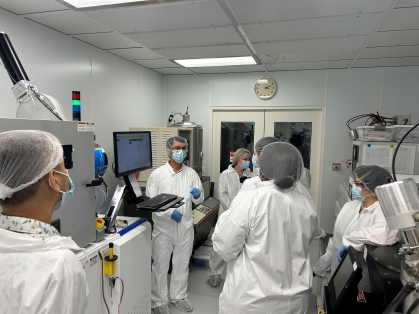 A group of six people are in a lab. They are all wearing white protective suits, masks, and hair covering.