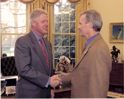 President Bill Clinton shakes hands with another gentleman in the Oval Office.