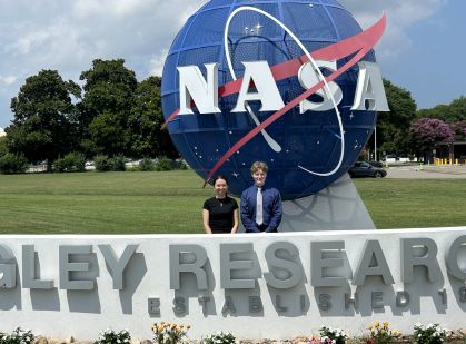 Woman wearing a black shirt standing next to a man wearing a blue shirt and white tie in front of a large statue for NASA