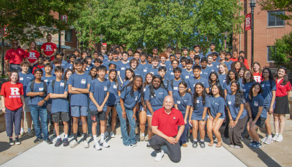 High school students wearing blue shirts posing outside with instructors wearing red shirts