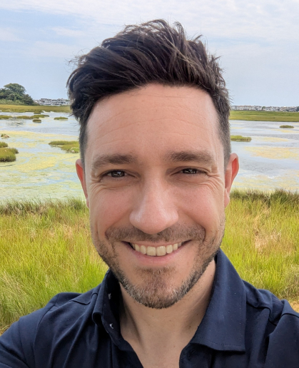 Man with bearded face, brown hair, marsh background