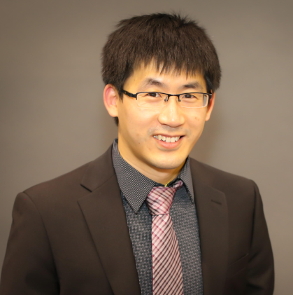 Man with short dark hair and glasses wearing dark blazer with tie