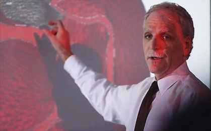 Man standing in front of a screen pointing to a section of a heart.