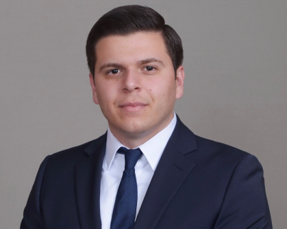 Man with short dark hair wearing a dark suit and tie