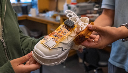 Two people hold a sneaker with electronics placed on top.