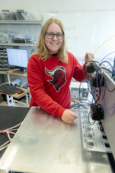 Smiling female student wearing glasses with blond shoulder length hair works in lab.