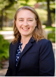 Headshot of female with long light brown hair wearing a dark suit jacket with a patterned blouse.