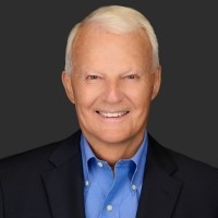 Headshot of male with short, white hair wearing a black suit jacket with a blue button down shirt.